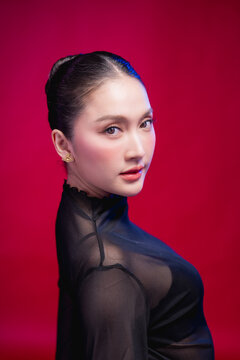 A captivating beauty portrait with the head tilted, direct gaze meeting the camera, elegant neckline and sleek updo against a deep red backdrop, blending allure with poise.
