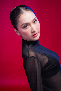 A captivating beauty portrait with the head tilted, direct gaze meeting the camera, elegant neckline and sleek updo against a deep red backdrop, blending allure with poise.