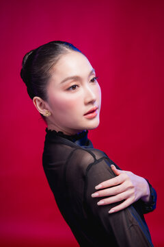 A captivating beauty portrait with the head tilted, direct gaze meeting the camera, elegant neckline and sleek updo against a deep red backdrop, blending allure with poise.