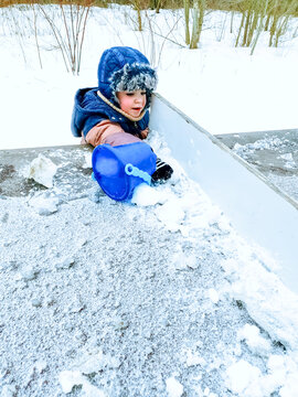 Cute toddler boy in warm winter clothes playing with snow outdoors. Concept of happy childhood, winter fun, family leisure, outdoor activities in cold weather, and seasonal recreation.
