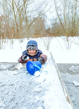 Cute toddler boy in warm winter clothes playing with snow outdoors. Concept of happy childhood, winter fun, family leisure, outdoor activities in cold weather, and seasonal recreation.