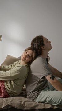 Portrait of young Caucasian woman sitting back to back with young adult Caucasian man, looking at camera. Visual suitable for dating app campaigns or relationship counseling advertising, vertical