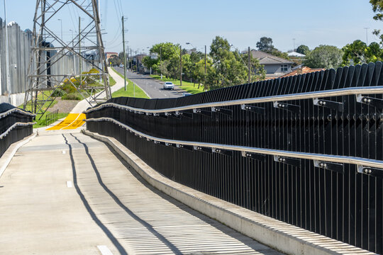 Elevated Federation Trail shared-use overpass, featuring modern safety balustrades, handrails running alongside high-voltage transmission towers and suburban roads. Yarraville, Melbourne, Australia