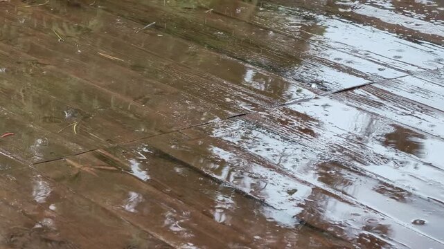 Rain drops falling on wet wooden deck surface, water droplets on weathered brown planks, outdoor veranda terrace in rain, precipitation on wood texture