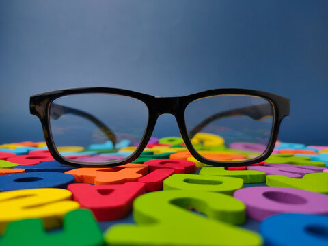 Black framed eyeglasses rest directly on a field of scattered colorful wooden alphabet letters and numbers