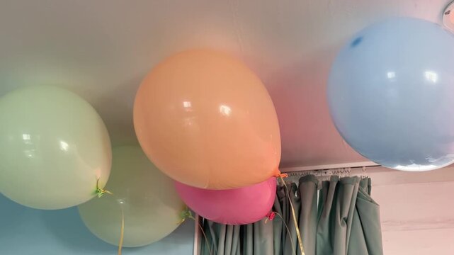 cinematic shot of colorful pastel balloons floating against a white ceiling in a bright room