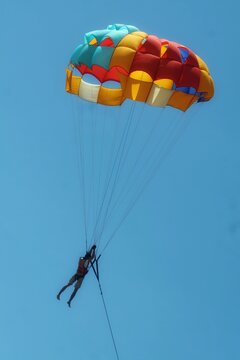 Colorful parasailing parachute carrying a person high in the clear blue sky.