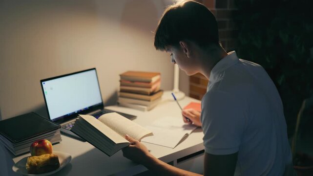 Dedicated youth reading literature at the illuminated home desk.