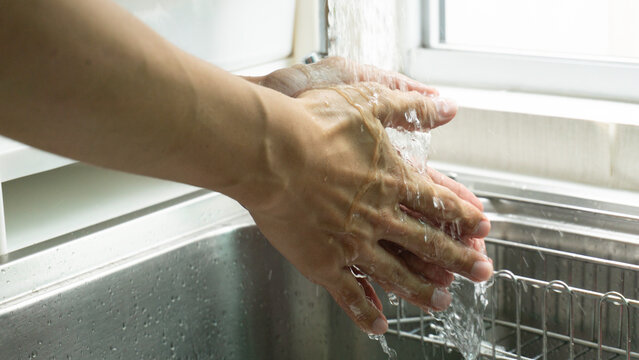 Close up of person washing hands with water in the kitchen sink. concept Hand hygiene routine for virus protection and cleanliness.