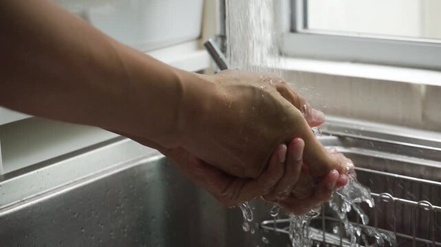 Close up of person washing hands with water in the kitchen sink. concept Hand hygiene routine for virus protection and cleanliness.