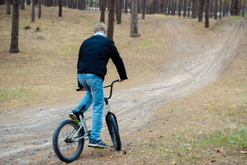 Fototapeta premium Young man riding a bmx bike on a dirt path through a pine forest in autumn