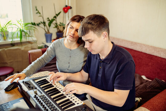 A teacher guiding a young teenage boy playing a digital synthesizer at home
