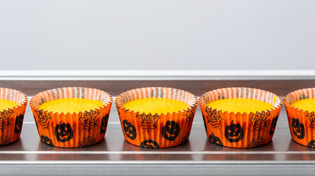 Festively Decorated Halloween Cupcakes in Orange Wrappers on a Baking Tray Ready for Decoration