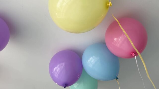 cinematic shot of colorful pastel balloons with ribbons floating gently against a white ceiling in a bright room