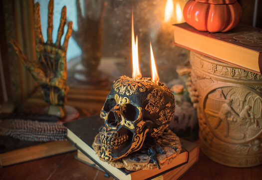 Maya carved skull candle with burning flames on old spell book, pagan ritual altar and esoteric concept 