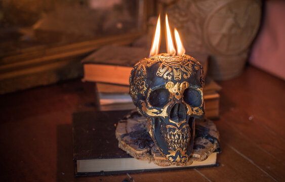 Maya carved skull candle with burning flames on old spell book, pagan ritual altar and esoteric concept 