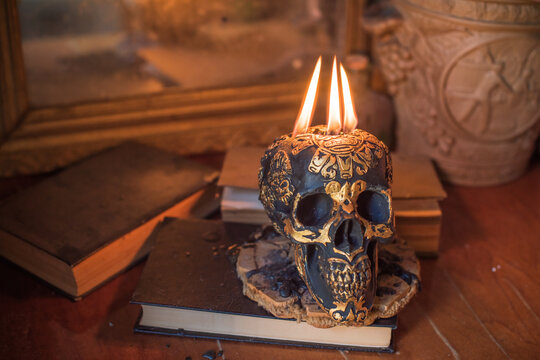 Maya carved skull candle with burning flames on old spell book, pagan ritual altar and esoteric concept 