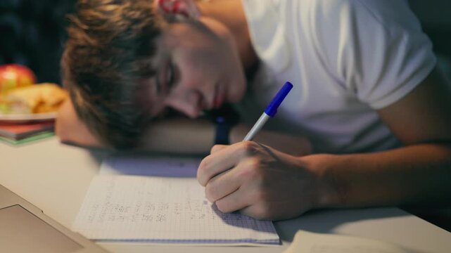 Exhausted youth sleeping on his notebook while doing academic homework.