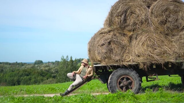 Highly engaging commercial ready video of a relaxed male farmer sitting on a hay wagon, nodding his head to the rhythm of music and enjoying a summer day.