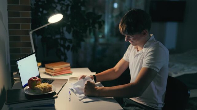 Frustrated teen youth crumbling paper failing a difficult late night homework.