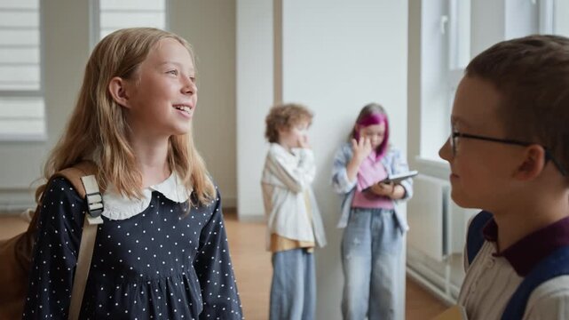 Caucasian schoolgirl talking with classmate in school hallway while students interact with digital tablet in background. Useful for educational projects, e-learning promos, back to school ads