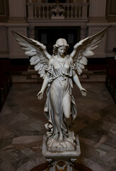Fototapeta premium Spirituality and religion concept marble angel statue with wings spread in a church interior for funeral memorial and peace themes in architecture