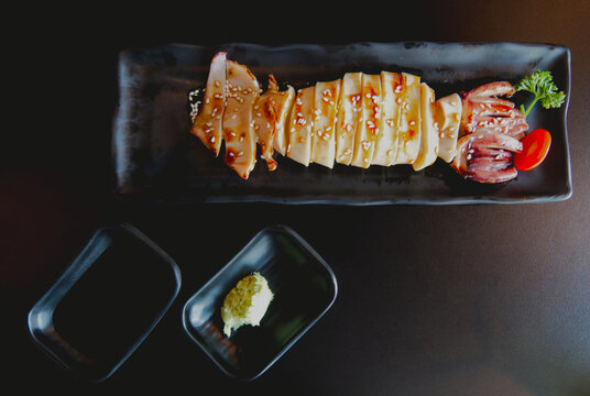 Grilled squid with teriyaki sauce and sesame seeds served with wasabi on a black plate.