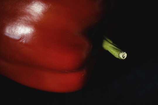 Macro shot of ripe red bell pepper with vibrant green stem in moody lighting on dark background. Fresh raw vegetable for organic recipes, culinary menus, nutrition, and healthy eating.