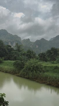 Tranquil river meanders through dense tropical jungle with towering mountains under a cloudy sky.