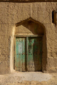 Weathered green wooden door set within an arched mudbrick doorway, Ad Dakhiliyah Region, Al Hamra, Oman