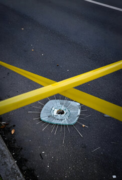 Crime scene investigation and forensic evidence, shattered glass on asphalt road with yellow caution tape marking a restricted area for police inquiry