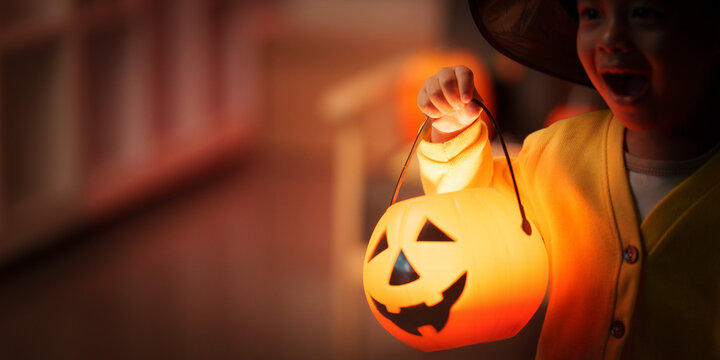 Cute young boy holding glowing pumpkin lantern bucket for Halloween trick or treating