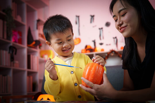 Asian mother and son painting pumpkin together for Halloween decoration at home