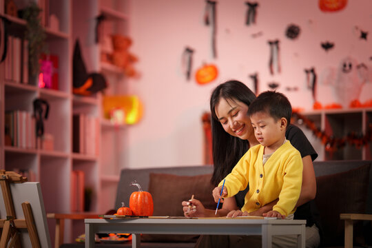 Asian mother and young son painting Halloween crafts together at home