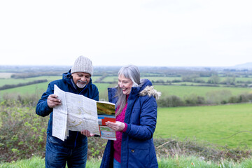 Obraz premium Smiling elderly white man and woman reading a map outdoors in countryside