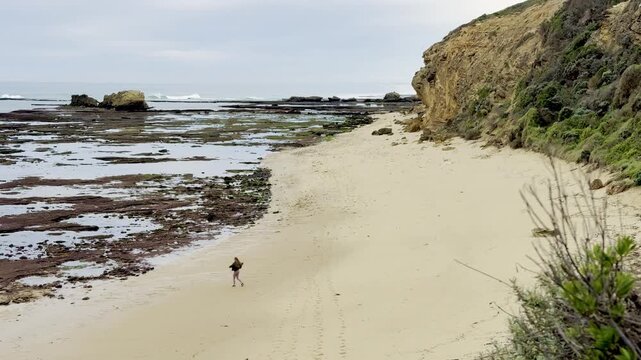 A happy girl runs along the empty Gunnamatta Beach, with stunning rock pools, raw cliffs and waves, near Cape Schanck, Mornington Peninsula, Melbourne, Victoria, Australia.
