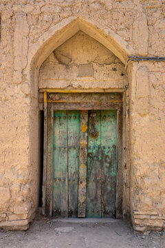 Weathered teal painted wooden door with a carved decorative panel set in a mudbrick archway, Ad Dakhiliyah Governorate, Birkat Al Mouz, Oman