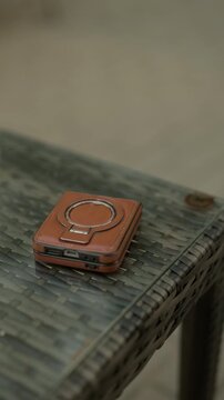 Brown leather compact case with metal ring resting on woven rattan table in soft light