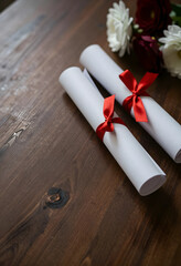 Obraz premium Graduation and academic achievement, two rolled diplomas with red ribbons on a rustic wooden table with flowers for celebration and success ceremony