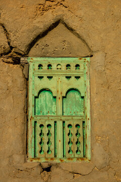 Close-up of a weathered green wooden window with a carved lattice shutter set into a cracked mudbrick wall, Dhofar Governorate, Mirbat, Oman