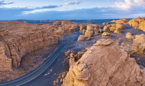 High angle aerial view of a paved highway winding through unique yardang landforms under a bright sky in Xinjiang, China.