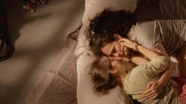 Young adult Caucasian couple lying in bed embracing and caressing face in top angle view. Suitable for romance campaigns, relationship storytelling and diversity advertising