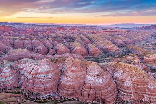 Colorful Danxia landforms and red sandstone rock layers stretching across vast hills under warm sunset light in Xinjiang.