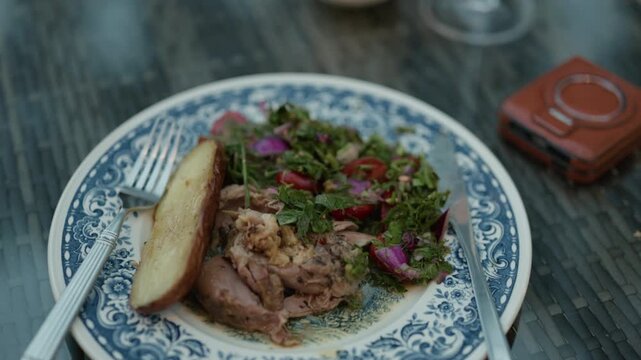 Roasted meat with herb salad and baked potato served on decorative blue patterned plate