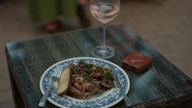 Gourmet dinner plate with roasted meat, salad and wine glass on outdoor table