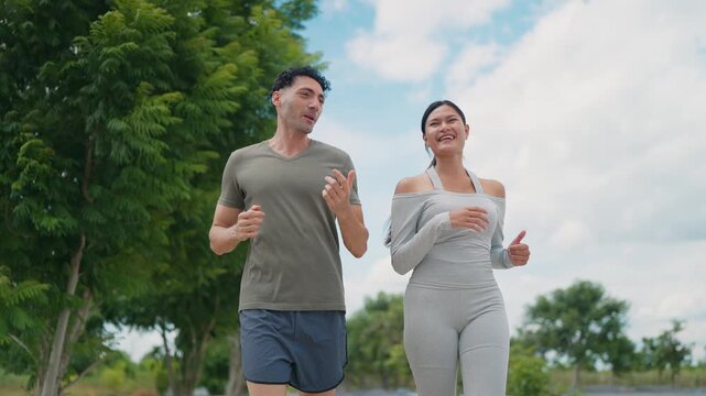 Two people jog side by side through a park. They smile and appear joyful, moving with ease. Trees and sky form a soft, natural backdrop