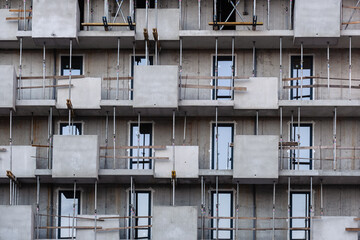 modern architecture residential building under construction facade with raw concrete geometric balconies steel scaffolding props wooden safety railings windows urban real estate development project © Soloviova Liudmyla