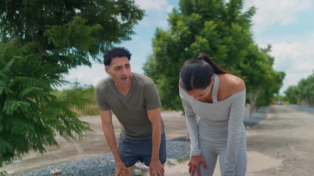 Couple breathes heavily after a brisk walk outdoors. Woman smiles, man looks tired but happy. Green trees line a sunlit path