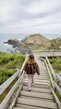 girl walks along the wooden coastal footpath overlooking the ocean at Cape Schanck, whale-watching spot with its own rock pools, near Fingal Beach, Melbourne, Mornington Peninsula, Victoria, Australia