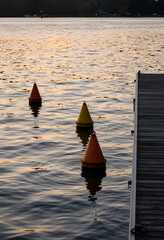 Fototapeta premium Marine safety and navigation, colorful buoys floating in calm lake water near wooden pier at sunset for maritime travel and water recreation